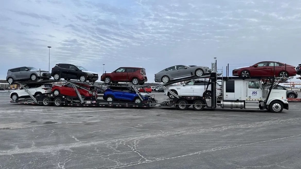 A loaded JDS car carrier on a dealer staging lot