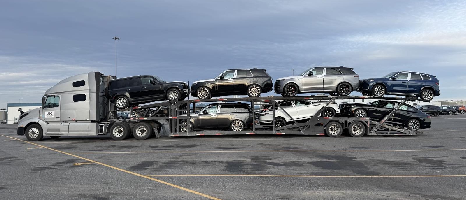 A JDS carrier loaded with luxury SUVs and sedans on a staging lot